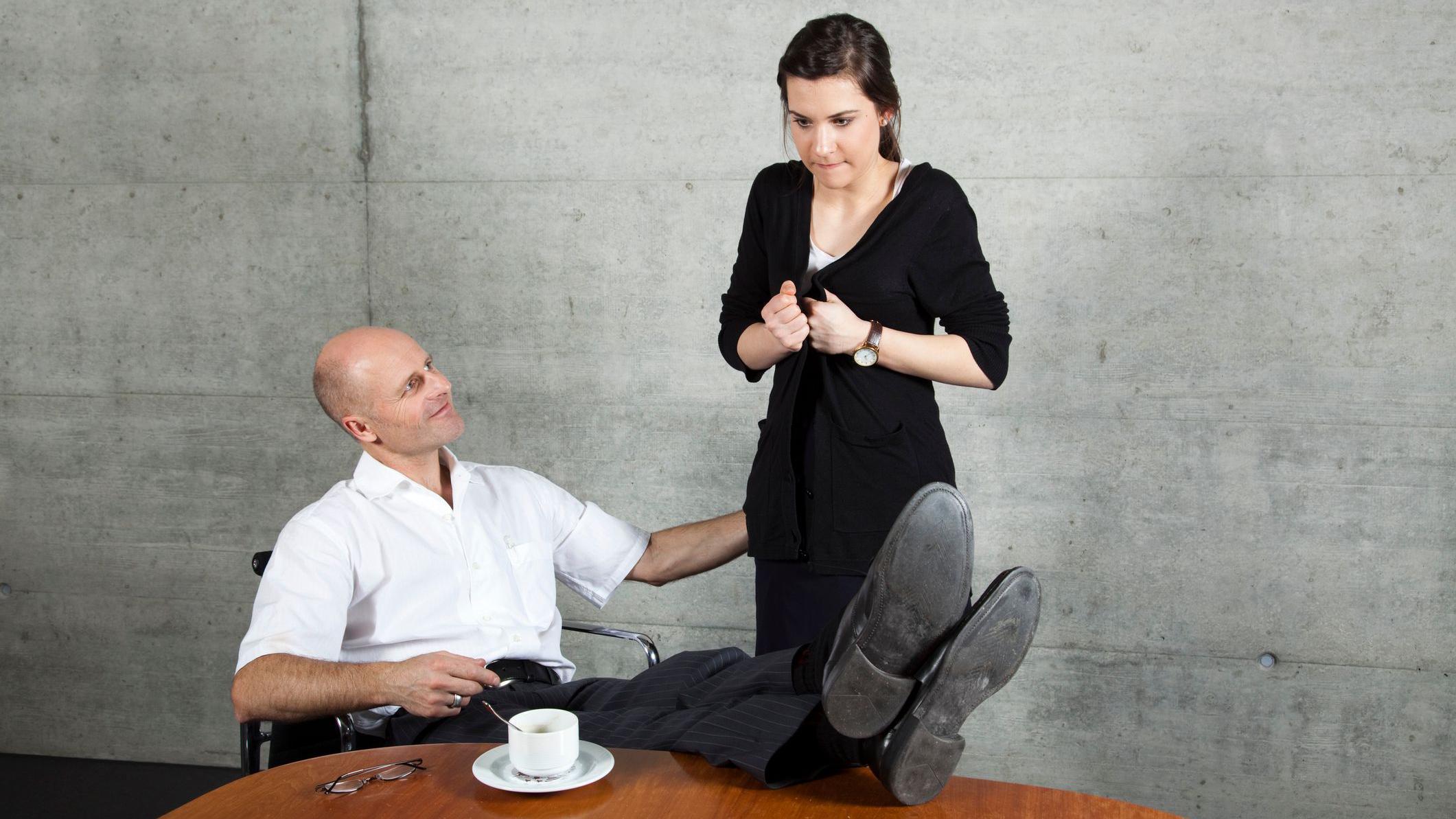 Homem sentado com os pés sobre a mesa toca nas nádegas de uma mulher que parece ser sua assistente, que mostra uma expressão assustada