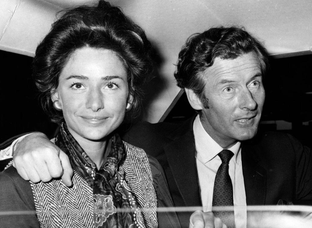 Una pareja dentro de un automóvil. El hombre tiene el brazo sobre el hombro de la mujer, que está mirando directamente a cámara.