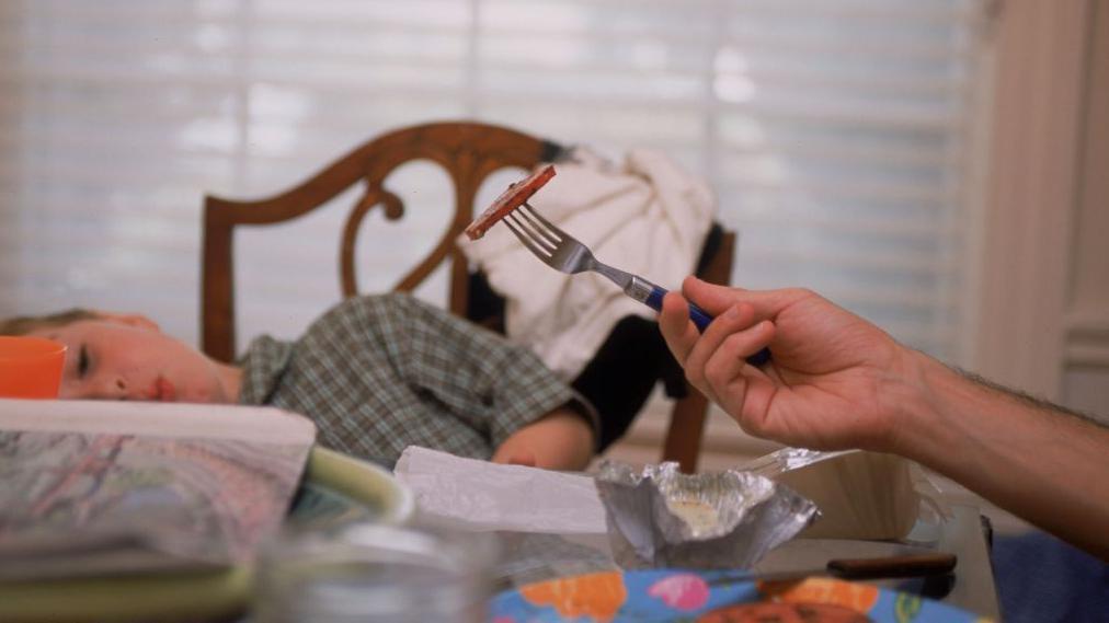 dečak se krije od viljuške na kojoj je zalogaj hrane koju druži odrasla osoba