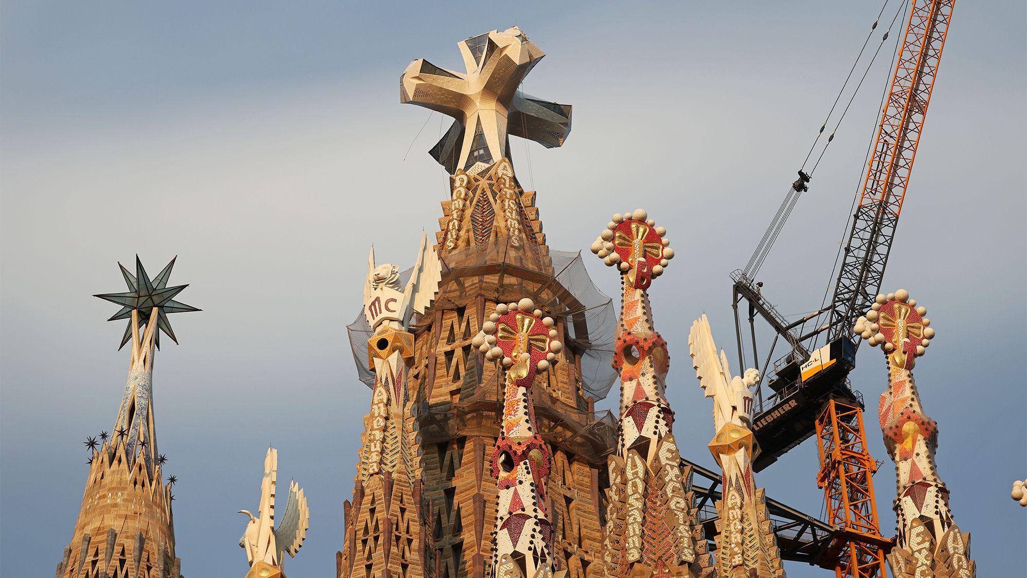 Una foto de las cimas de varias torres ornamentadas, con la más grande en el centro, que tiene una cruz en su parte superior.