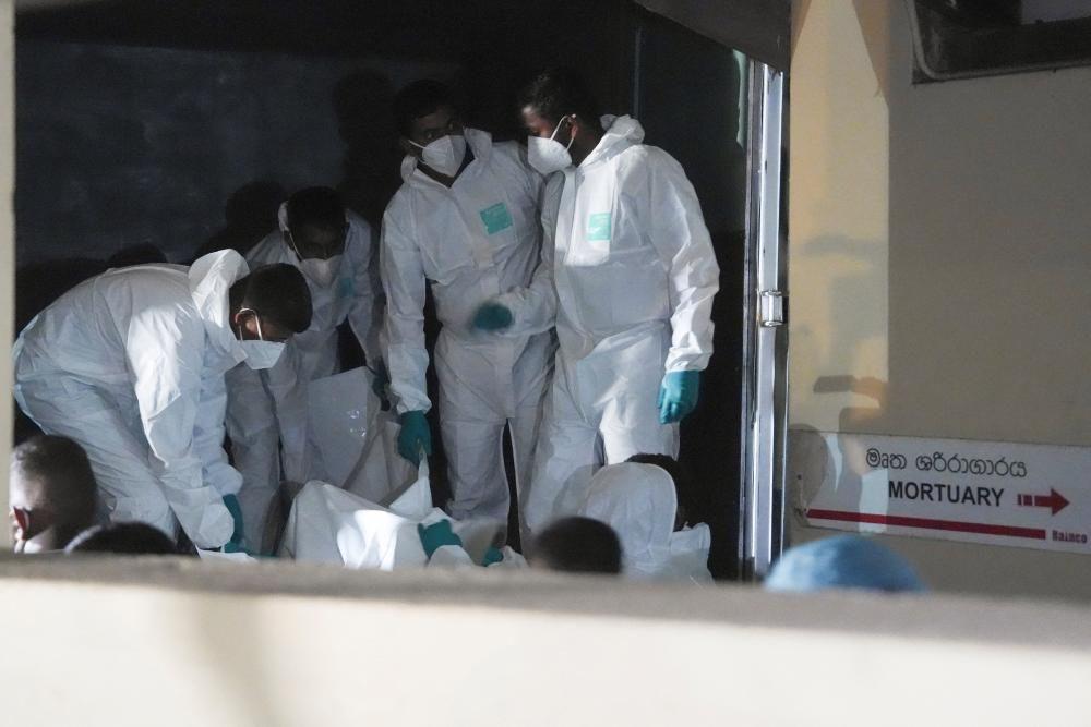 Varios hombres vestidos con trajes protectores mueven cuerpos recuperados del buque iraní hundido