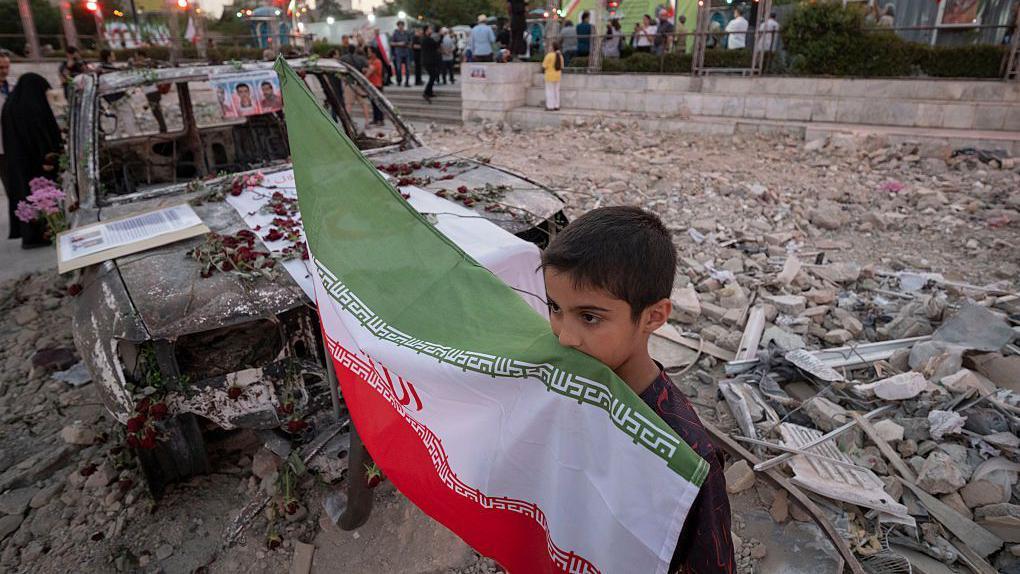 طفل إيراني يحمل علم بلاده وسط الدمار