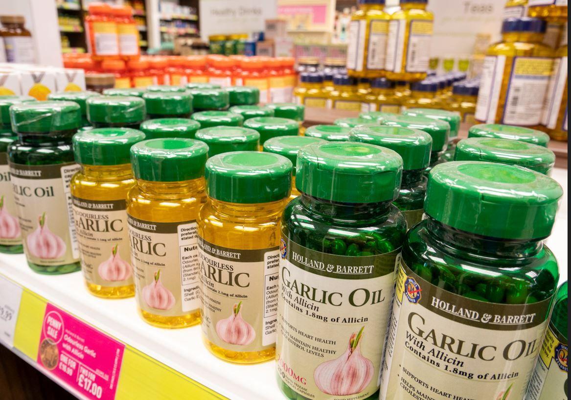 Yellow bottles containing garlic oil and green bottle containing garlic capsules stacked up in a rack in UK