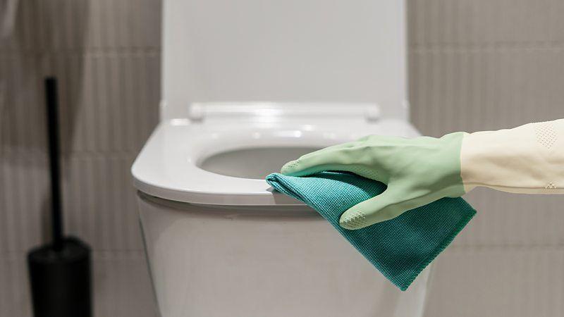 Pessoa limpando vaso sanitário com luva e pano