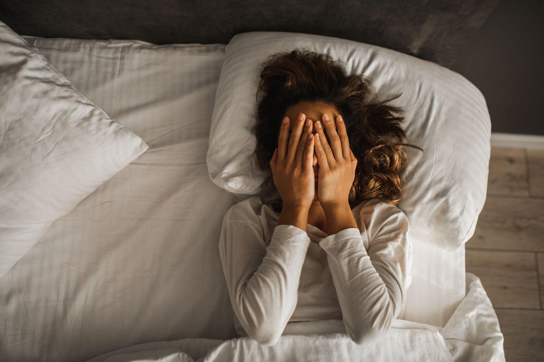 Mulher deitada na cama cobrindo o rosto com as mãos