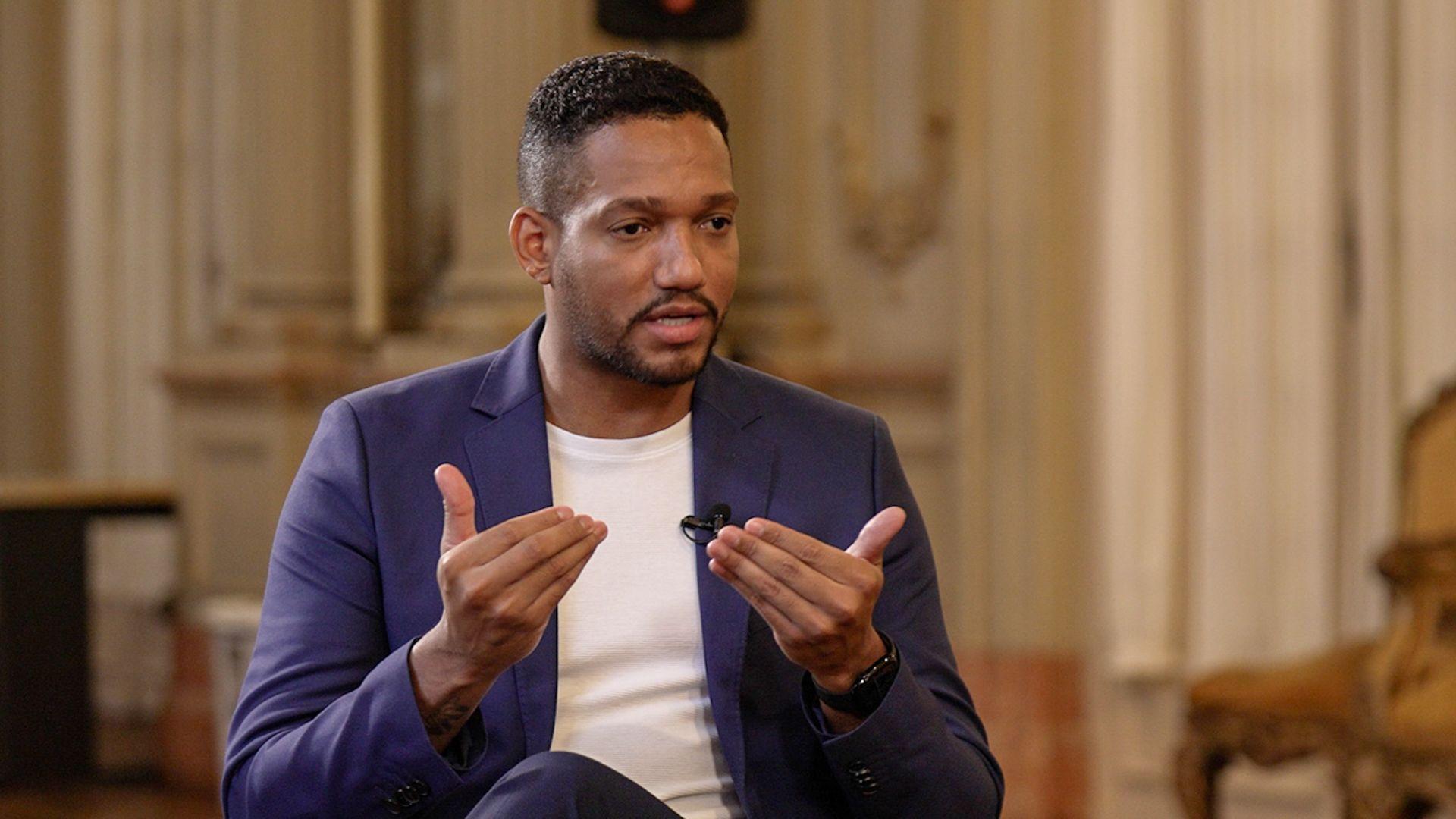 Rick Azevedo gesticulando durante entrevista à BBC. Ele veste terno azul e camiseta branca, e usa um cavanhaque e cabelo curto, raspado dos lados