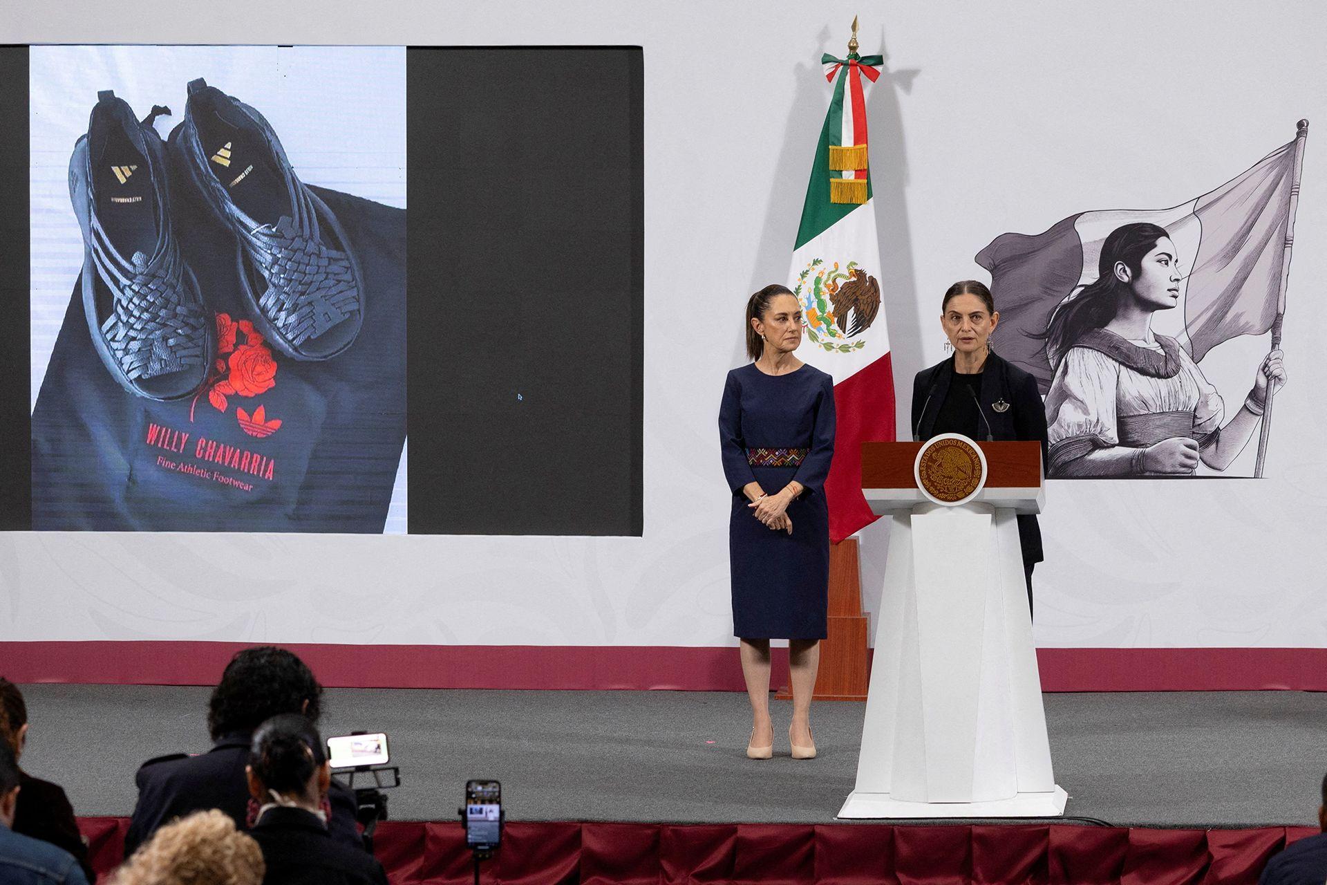 A vice-ministra de Desenvolvimento Cultural do México, Marina Núñez Bespalova, fala em um púlpito no palco, com os tênis da Adidas expostos ao fundo e repórteres em primeiro plano