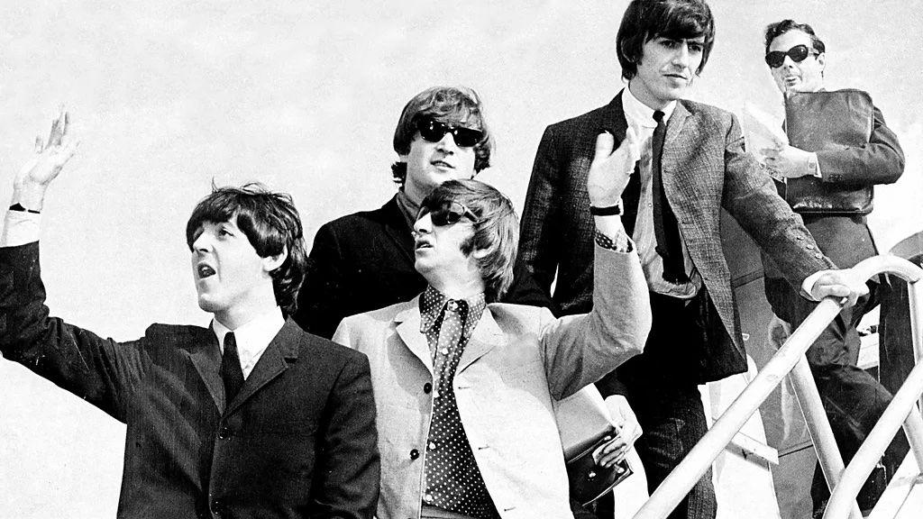 Beatles e Epstein acenando para as pessoas em cima de uma escada