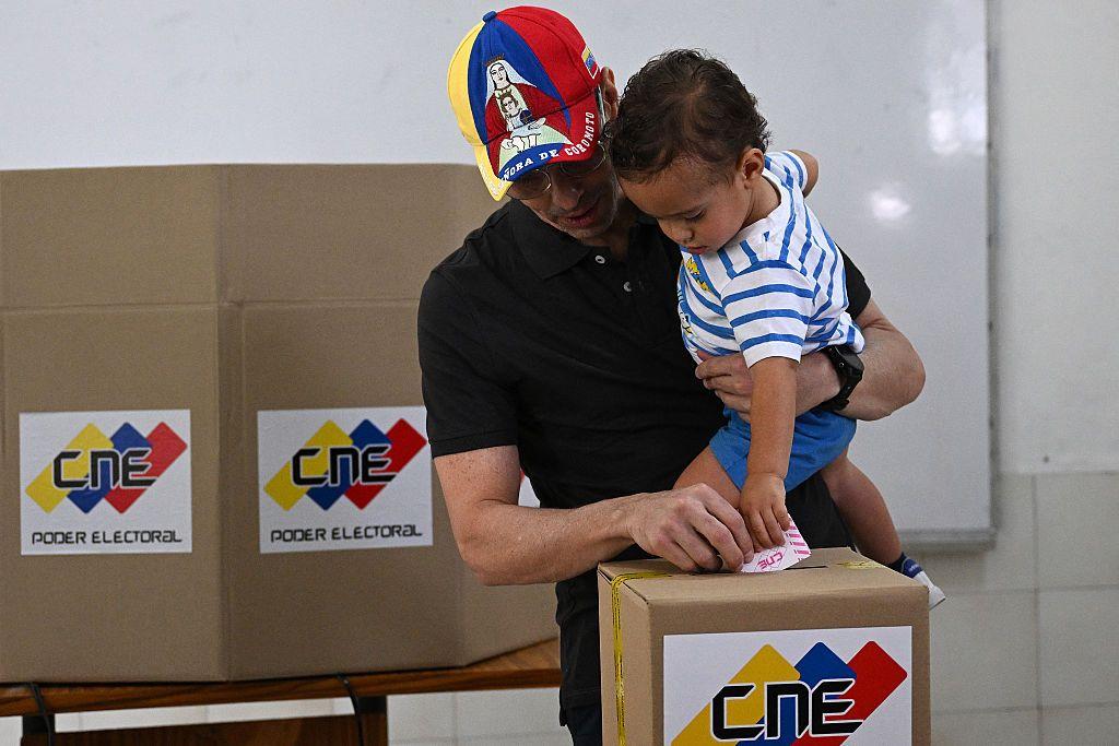 El líder opositor venezolano y candidato a diputado Henrique Capriles Radonski emite su voto mientras sostiene a su hijo en un centro de votación durante las elecciones regionales en Caracas el 25 de mayo de 2025.