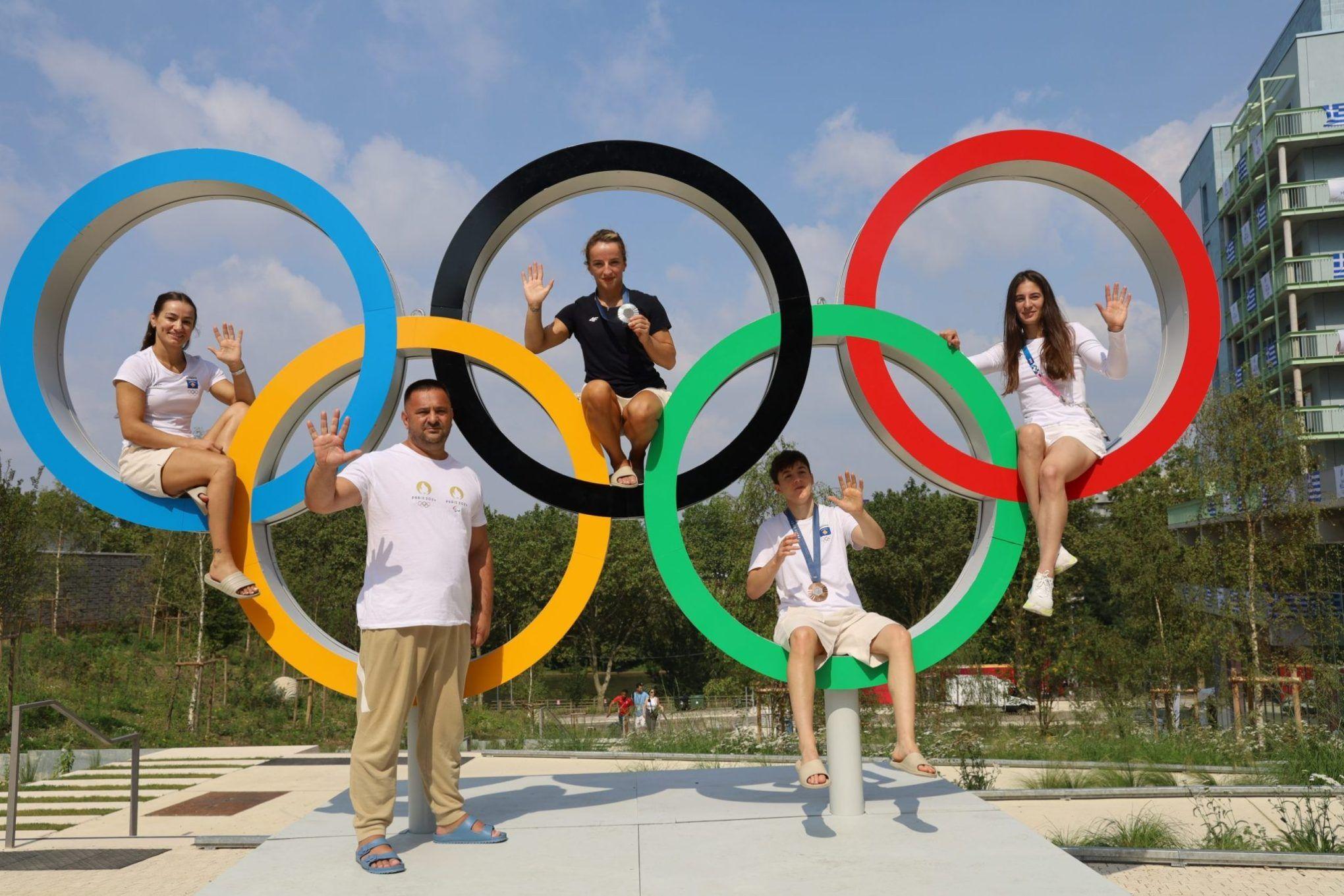 Cinco pessoas posando em meio a arcos olimpícos e com medalhas