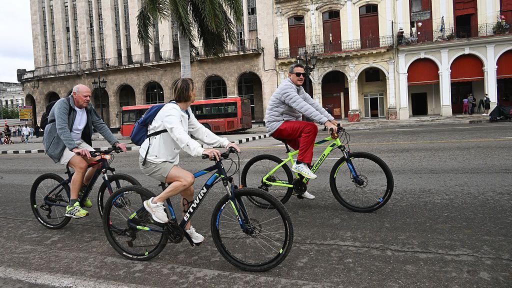 Tres turistas pasean en bicicleta por La Habana.