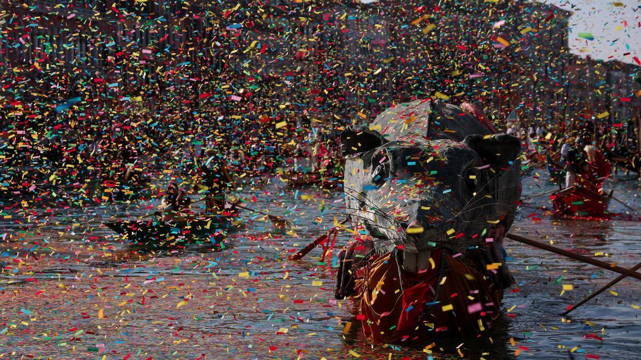 Konfete i trake padaju, a u krupnom kadru je veliki pacov na jednom od čamaca koji se kreće Velikim kanalom u Veneciji