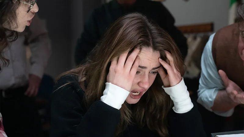 La actriz Grace Van Patten tiene las manos en las sienes en señal de desespero, mientras otros dos actores la interrogan, en la nueva serie de Disney.