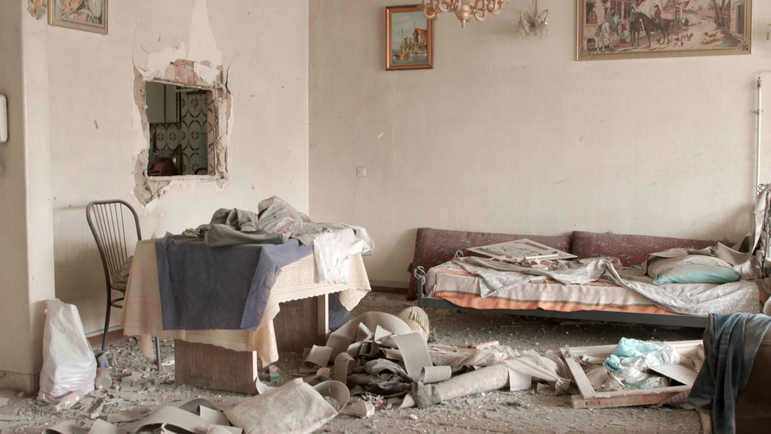 Una fotografía muestra el interior de un apartamento gravemente dañado, con escombros esparcidos por el suelo y un sofá y una mesa deteriorados.