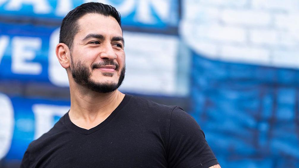 Abdul El-Sayed, vistiendo una camiseta negra, mira con una sonrisa hacia el lado derecho de la pantalla.