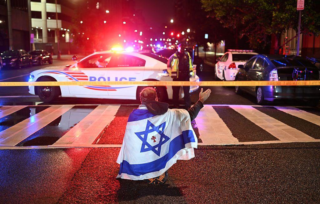Un hombre con la bandera israelí frente a unos coches de policía.