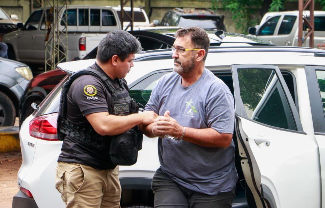 Un agente de policía saca a un hombre esposado de un coche.
