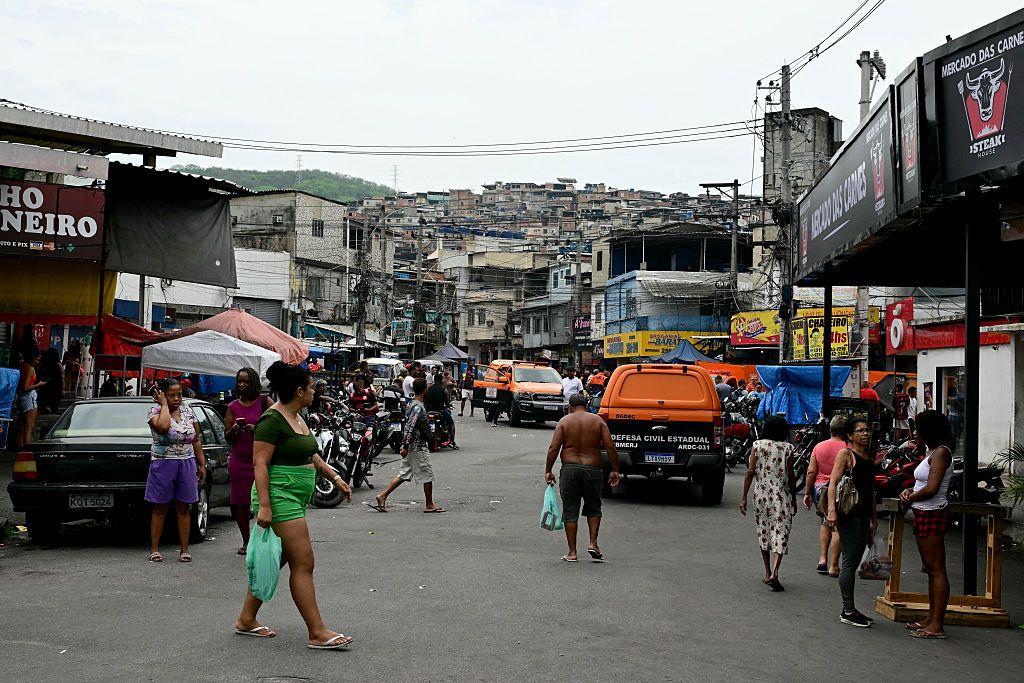 Pessoas caminhando e comércio em área plana da favela