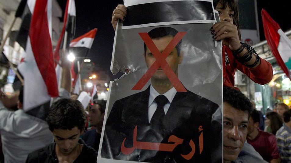 ما هي العقوبات المفروضة على سوريا؟ 4 متظاهرون يحملون صورة لبشار الأسد مكتوب عليها: "ارحل".