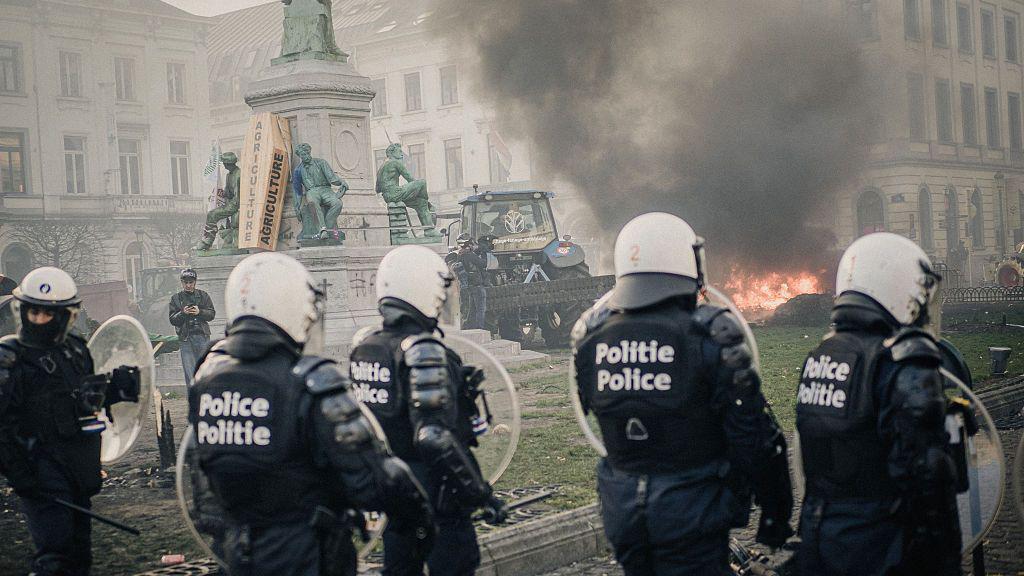 Protestas en frente de las instituciones europeas en Bruselas. Varios policias rodean un tractor y un fuego.