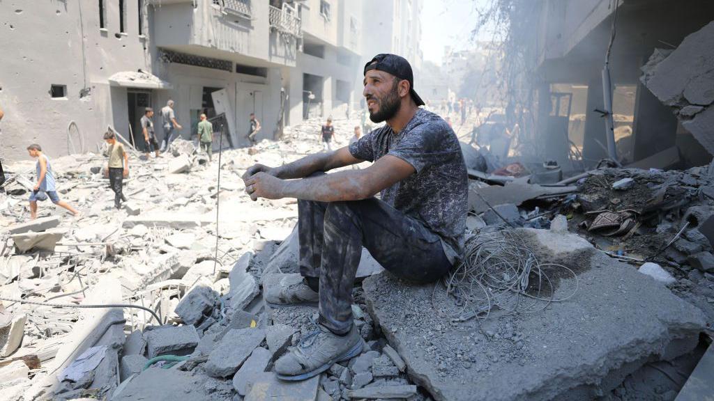 Homem sentado sobre escombros na Faixa de Gaza