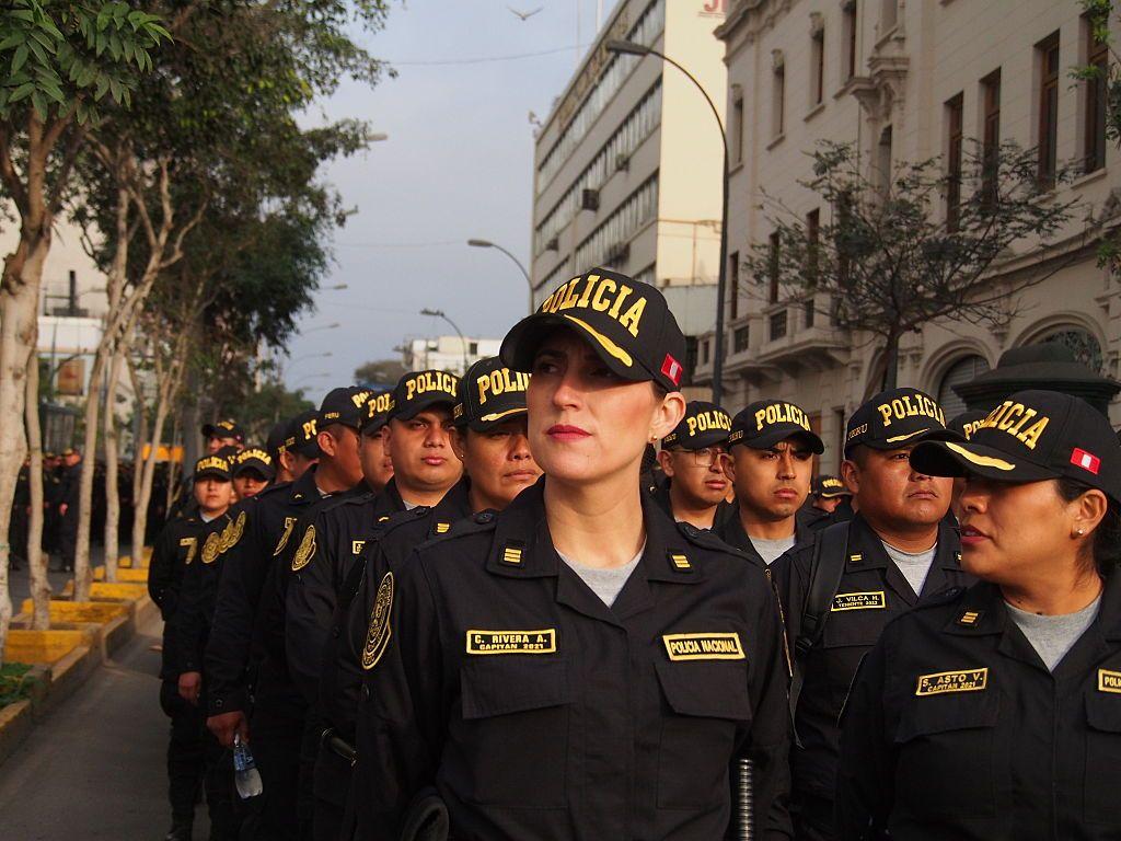Una mujer policía, en primer plano de una columna de agentes de la Policía Nacional del Perú, en una calle peruana.