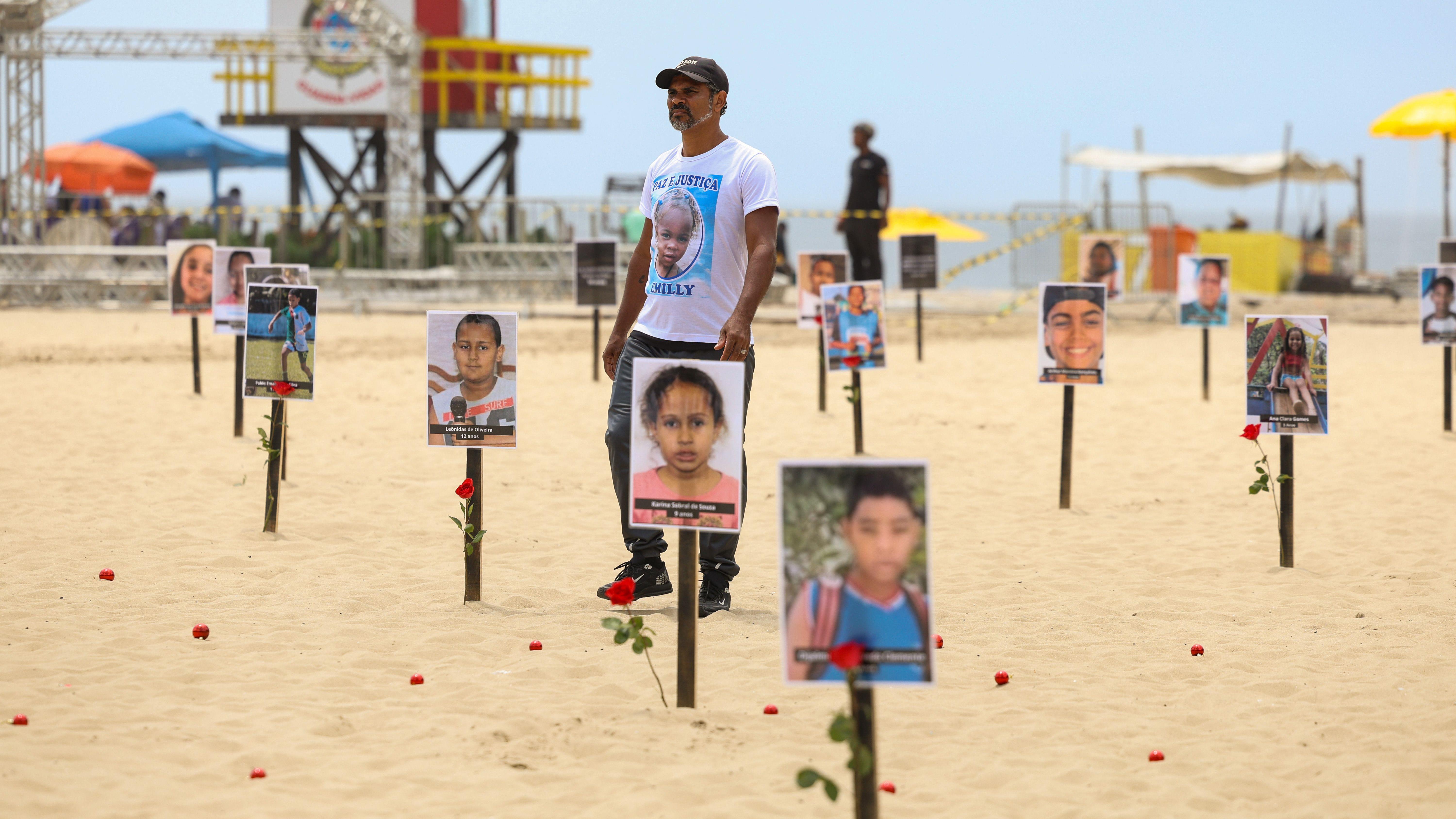 Diversas placas com fotos de crianças foram fincadas na areia da praia com rosas vermelhas.