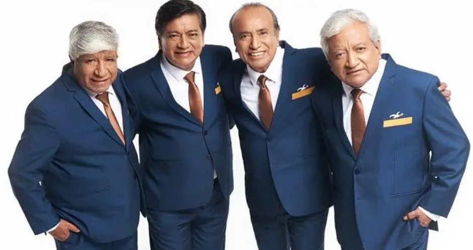 O grupo musical Agua Marina. Quatro homens posam juntos, sorrindo, usando ternos azuis com gravatas marrons e lenços dourados no bolso. Estão lado a lado, com os braços apoiados nos ombros uns dos outros, diante de um fundo branco.