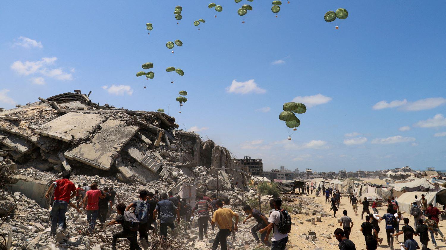 FILE PHOTO: Palestinians run towards parachutes carrying aid packages airdropped over northern Gaza Strip, August 7, 2025. REUTERS/Ebrahim Hajjaj/File Photo