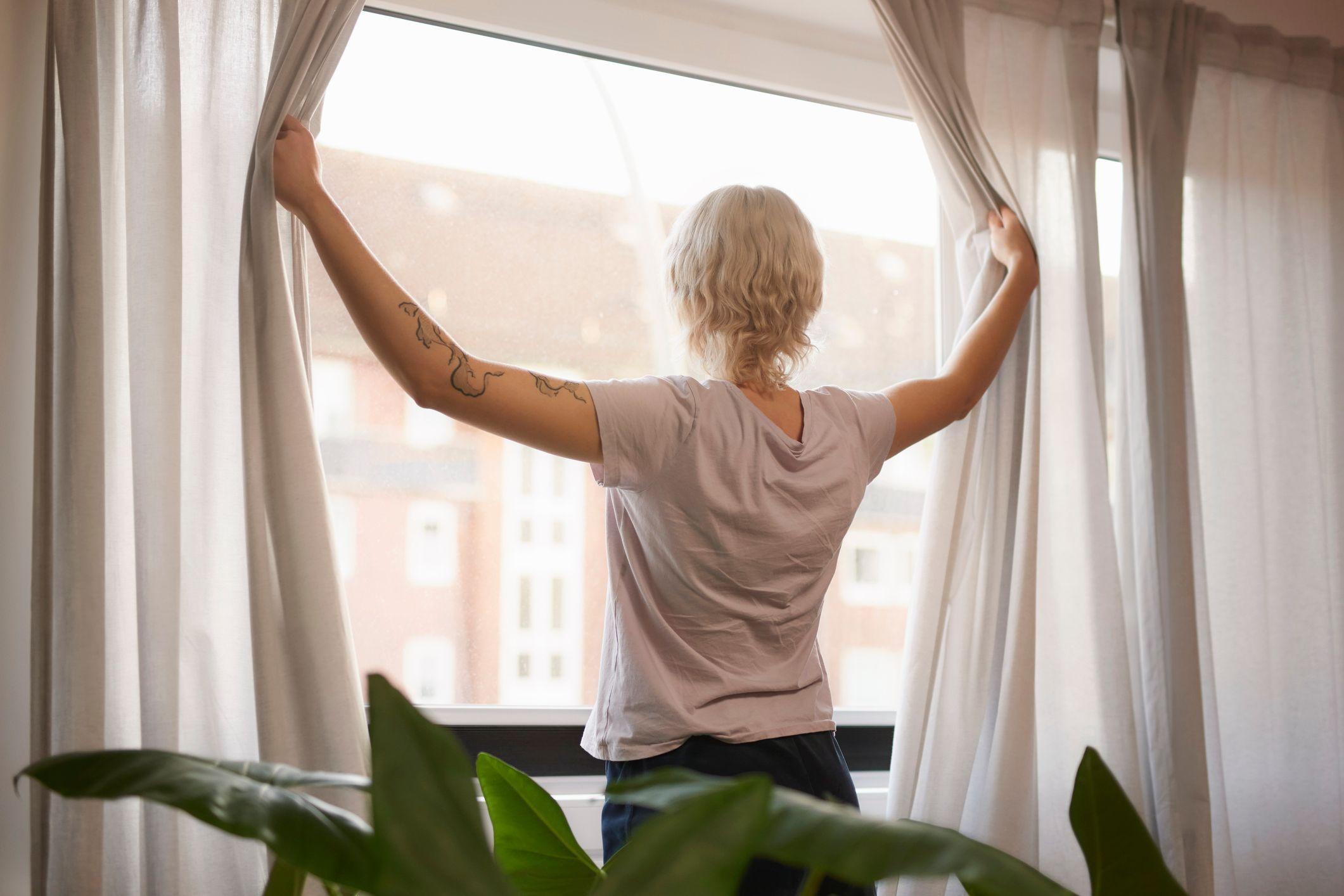 Una mujer abriendo las cortinas de su casa para recibir el sol