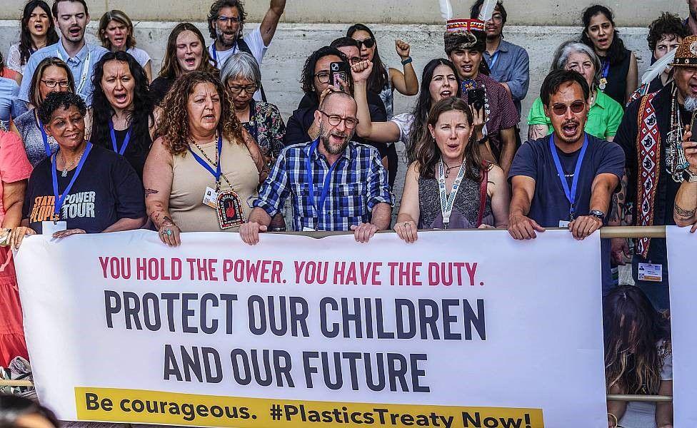 Activistas con un cartel que dice "Ustedes tienen el poder, ustedes tienen el deber. Protejan a nuestros niños y al futuro. Tengan coraje. ¡Un tratado sobre el plástico ahora!