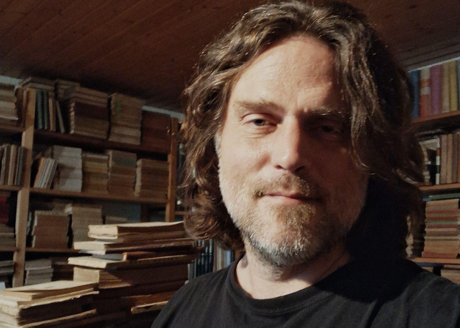 Un hombre en primer plano con libros detrás.