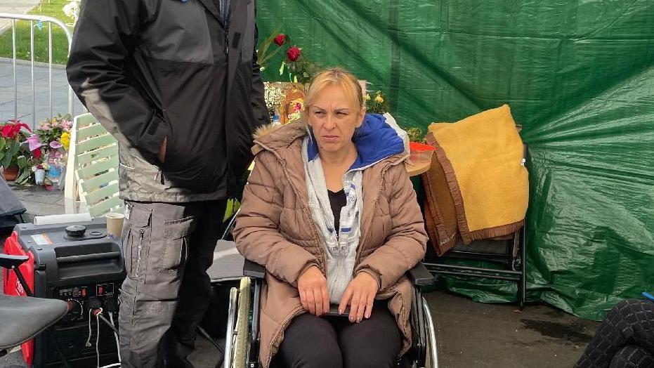 Dijana Hrka 15 dana štrajkuje glađu u Beogradu, tražeći istinu o sinu i još 15 ljudi koji su poginuli u padu nadstrešnice u Novom Sadu. Sedi u kolicima u smeđoj jakni i beloj dukserici