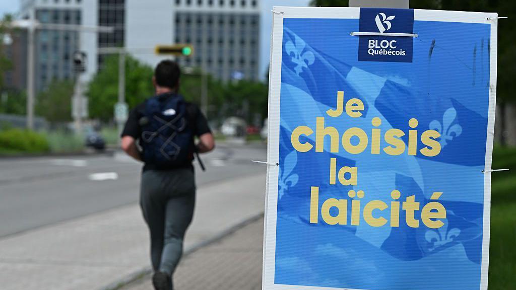 Homem caminha ao lado de um p&ocirc;ster de campanha pol&iacute;tica azul e amarelo, com os dizeres em franc&ecirc;s 'Escolho o laicismo', em Longueuil, no Canad&aacute;