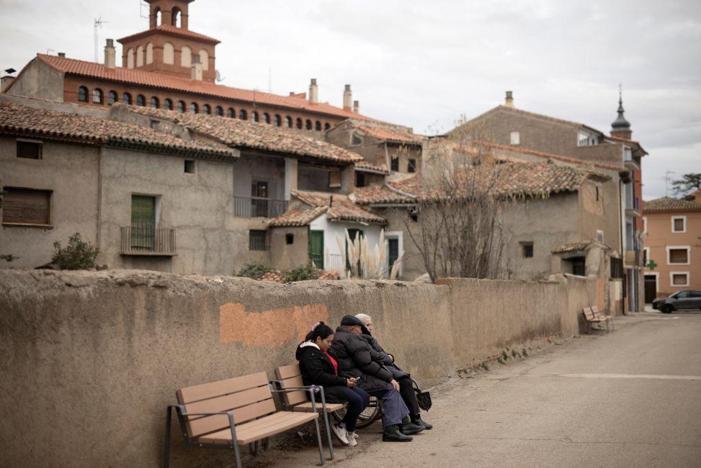 Dos ancianos y su cuidadora sentados en un banco de Burbaguena