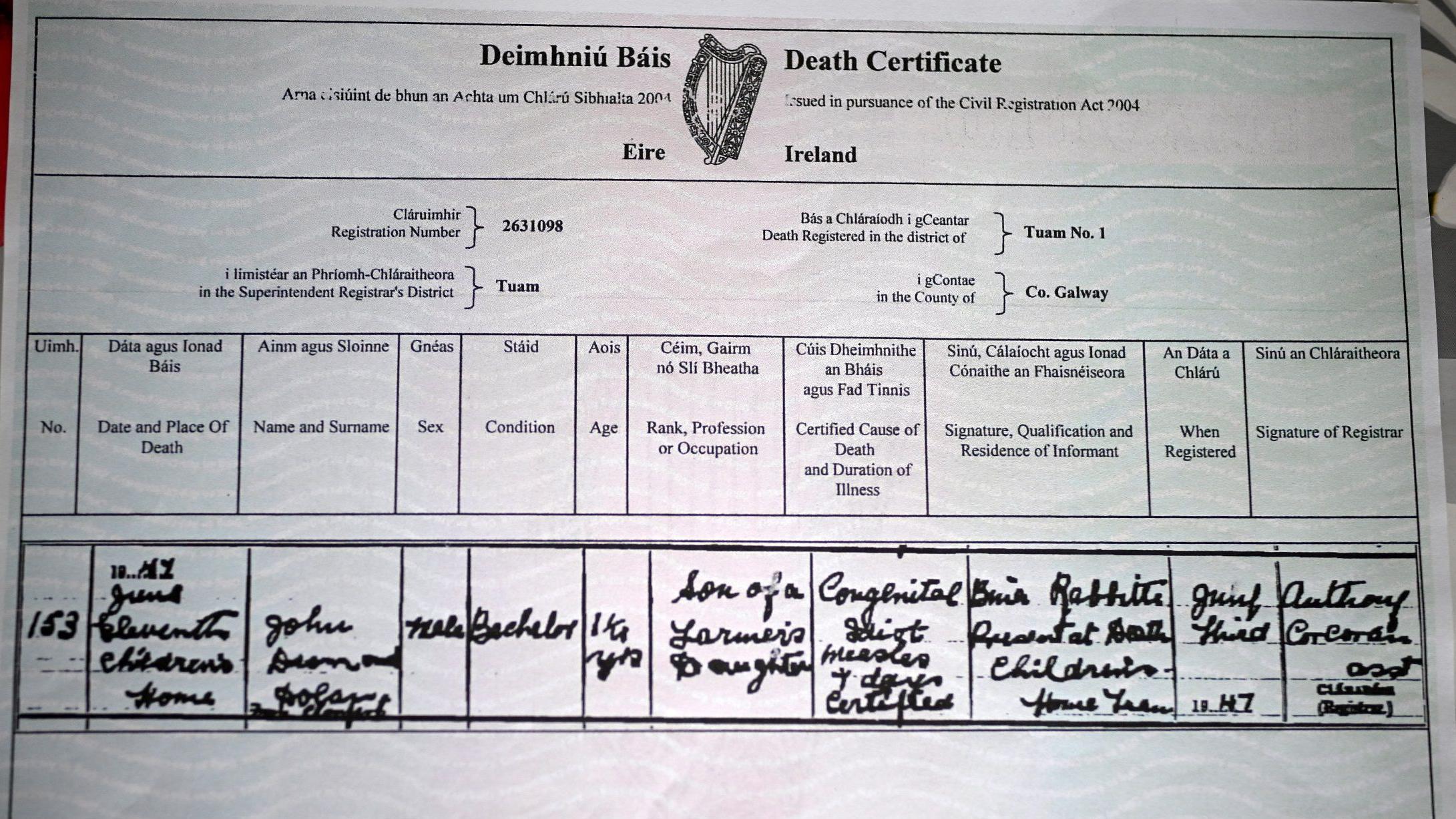 Primer plano de un certificado de defunción irlandés. Contiene una tabla de información que incluye nombre, fecha y lugar de fallecimiento, sexo, edad y otros detalles. La información está escrita en cursiva fluida y señala que el fallecido se llama John, tenía 16 meses y menciona "idiota congénito" y "sarampión" como causa de muerte.