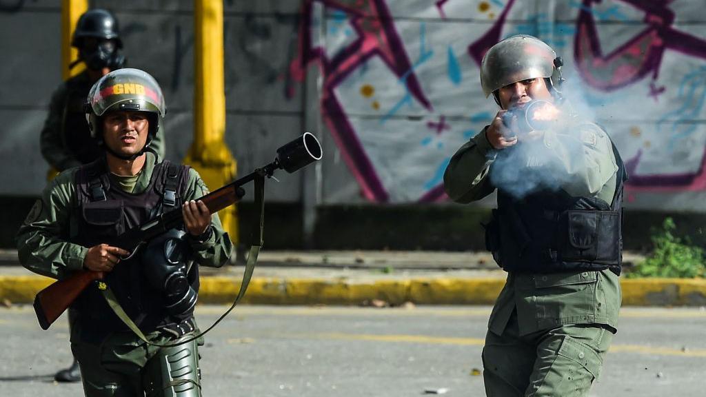 Agentes da Guarda Nacional Bolivariana vestidos de verde e usando capacetes disparam suas armas