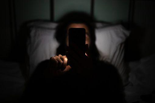 شخص محدق في هاتفه الخلوي في غرفة مظلمة