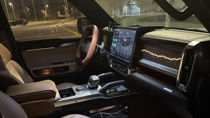 صورة من داخل السيارة حيث مقاعد ترتدي جلداً بُنيّ اللون، ولوحة تحكُّم مميزة وشاشة عرض كبيرة