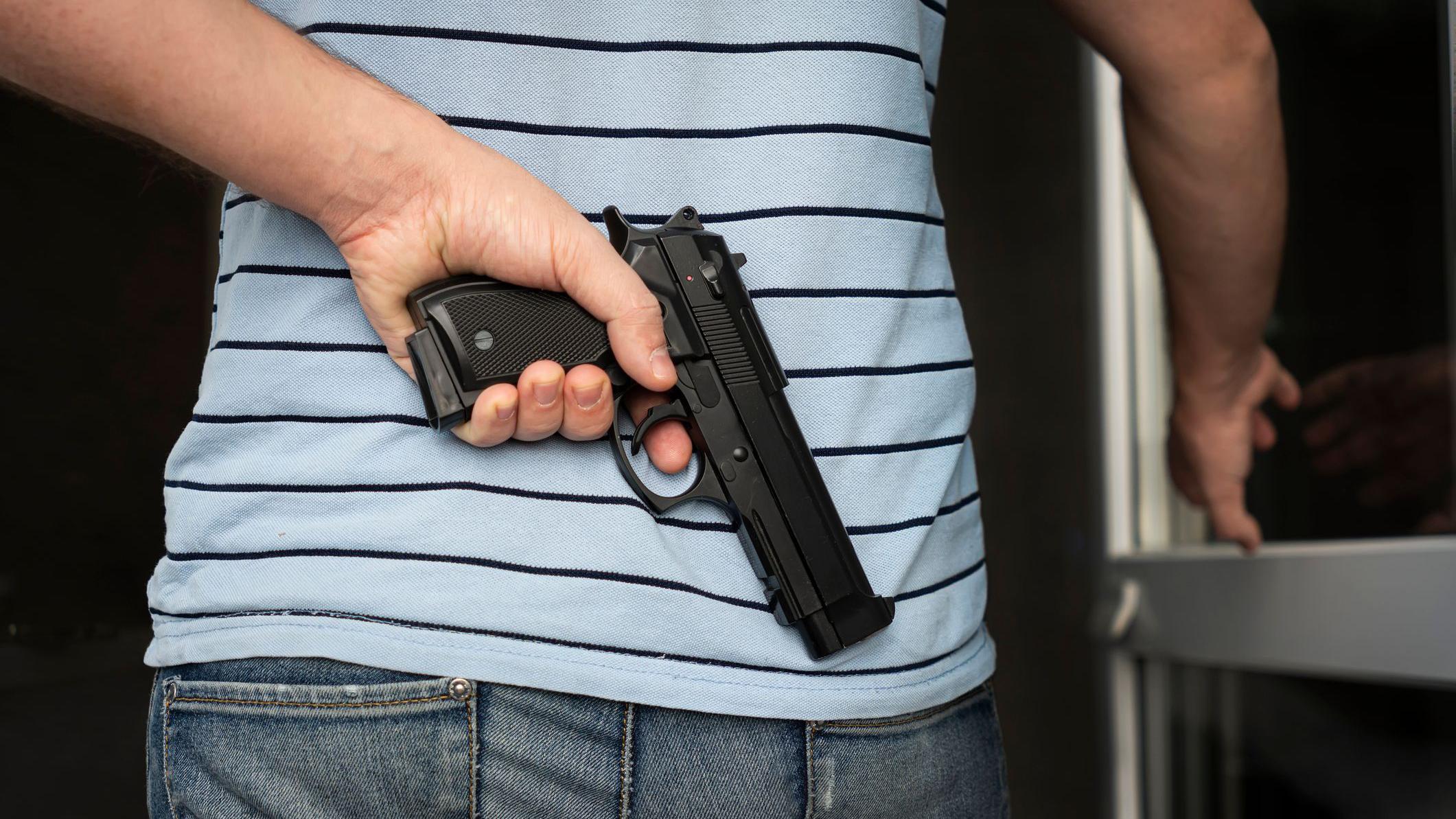 Un hombre esconde un arma en su espalda mientras abre una puerta