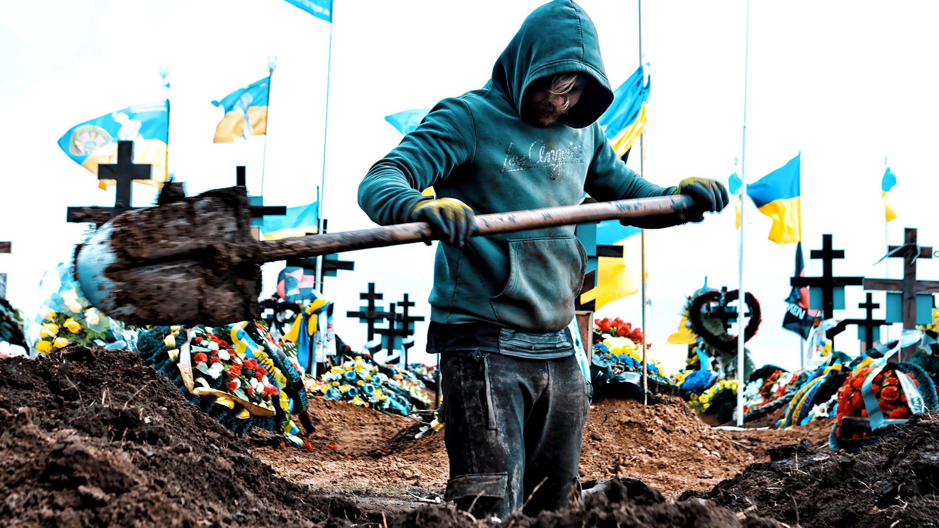 Zamrznuta ruska imovina: Šta hoće EU i zašto se Belgija protivi 1 Muškarac kopa grob na groblju u Odesi 16. marta 2024. Oko deset ukrajinskih zastava vijori se na belim jarbolima iza njih. Kopač groba u nosi tirkiznu duksericu sa kapuljačom, u rukama mu je lopata