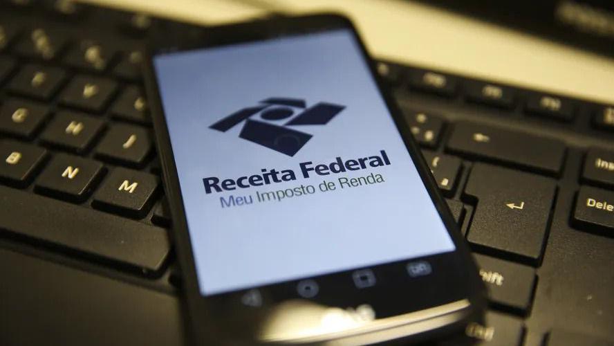 Celular com o logotipo da Receita Federal na tela, sobre um teclado de computador preto