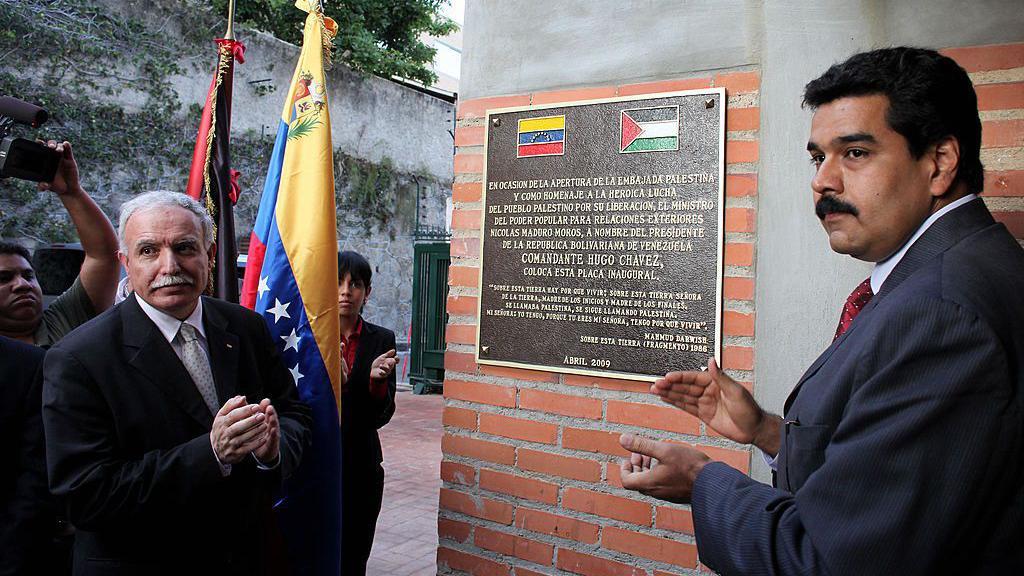 مادورو والمالكي يقفان على طرفي لوحة فيها علما فلسطين وفنزويلا على جدار سفارة فلسطين في كركاس في افتتاحها عام 2009. 