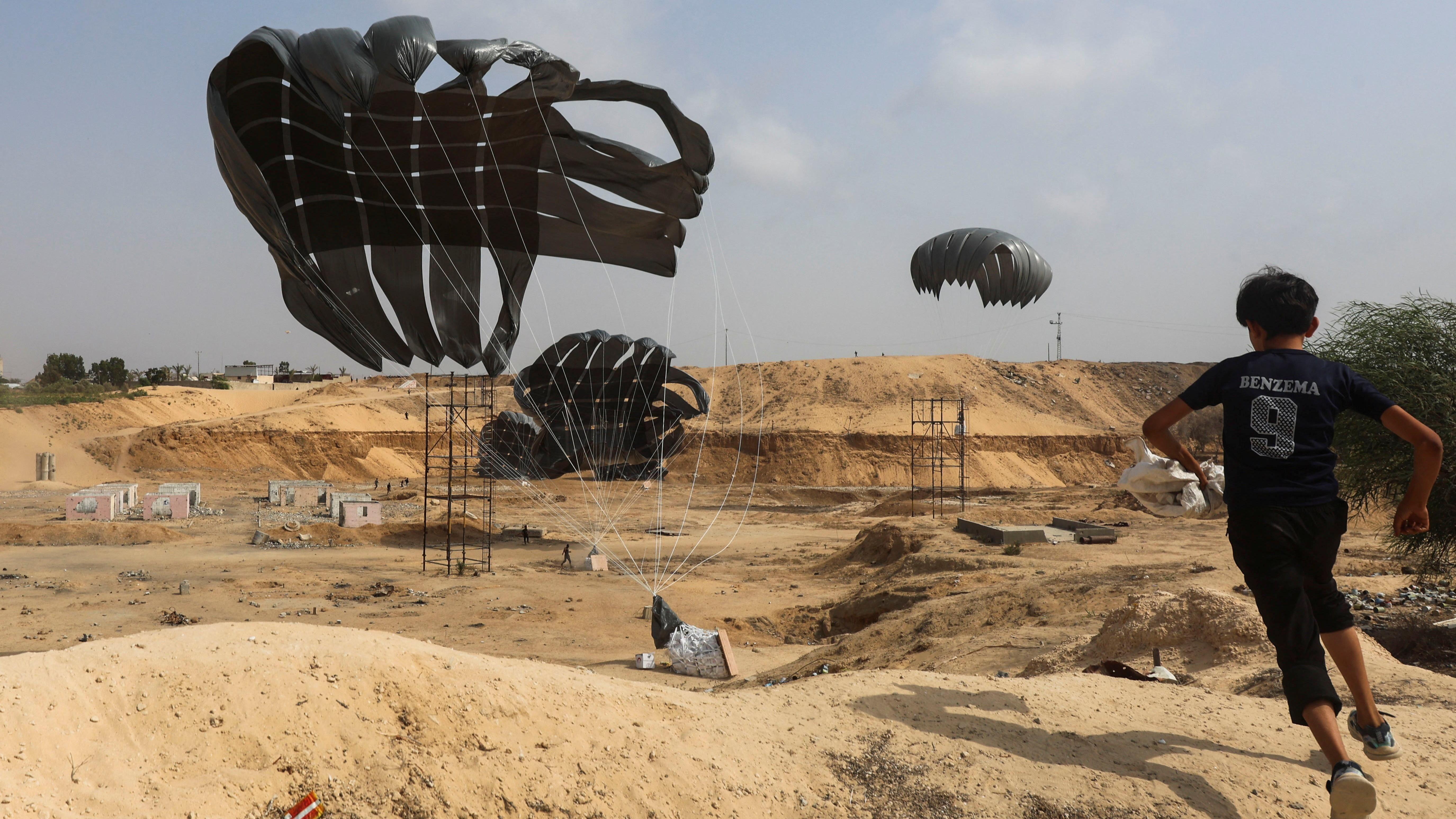Garoto com camiseta azul corre em busca de pacote de ajuda humanitária que chega com um paraquedas