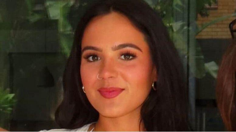 En la foto, Hen Howard aparece de los hombros hacia arriba sonriendo a la cámara. Lleva un pintalabios rosa brillante y tiene el pelo largo y oscuro.