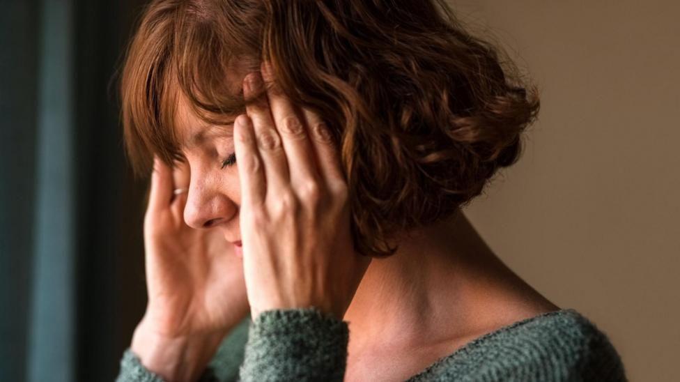 Una mujer de costado con las manos en sus sienes y los ojos cerrados