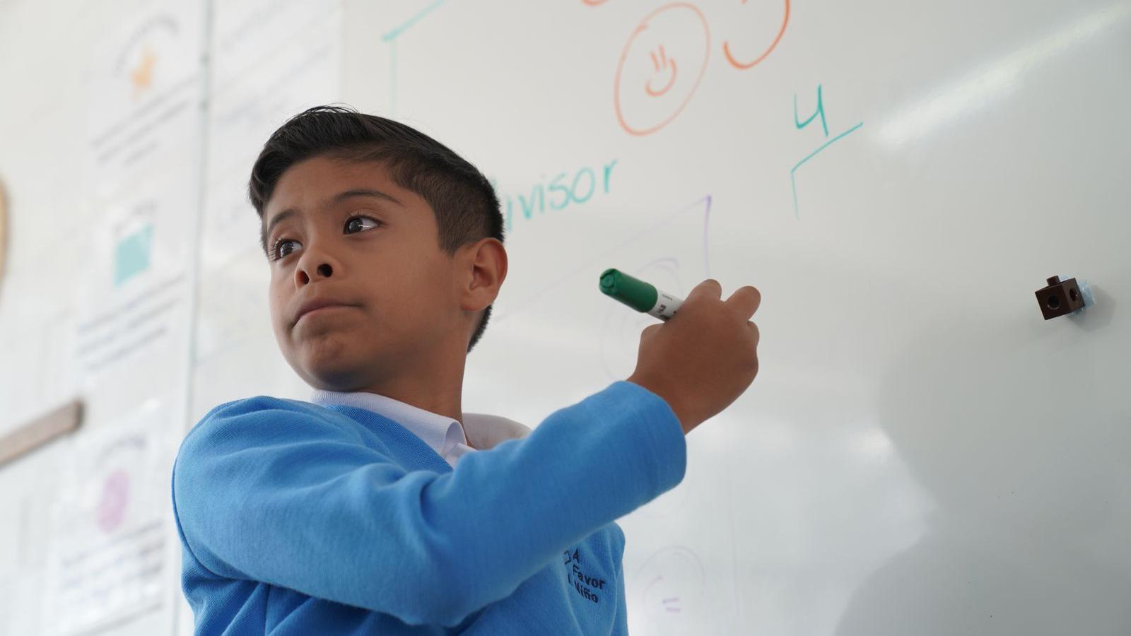 Un niño de la escuela "A favor del niño" escribe en la pizarra de clase.