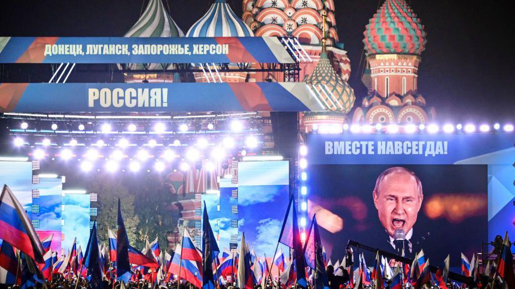 El presidente ruso, Vladímir Putin, visto en una pantalla gigante mientras se dirige a una multitud de seguidores en un mitin-concierto en la Plaza Roja de Moscú en 2022. Hay muchas banderas de Rusia entre el público. 