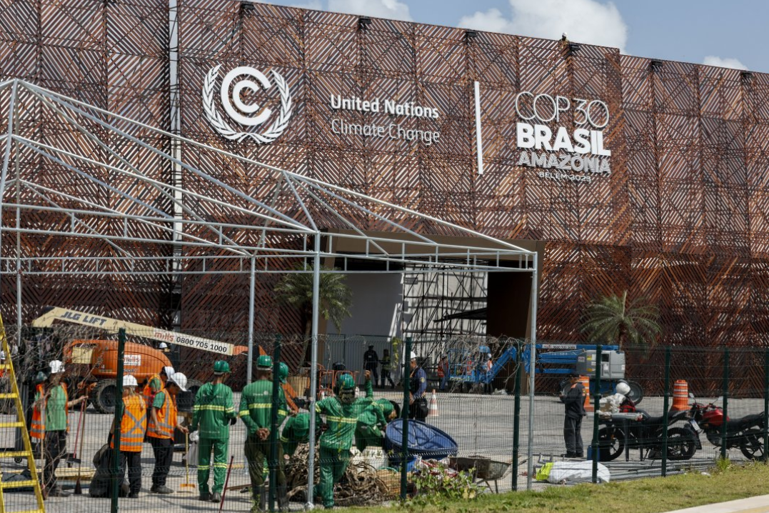 Operários trabalhando em frente a grande centro de convenções com logomarcas da ONU e da COP30