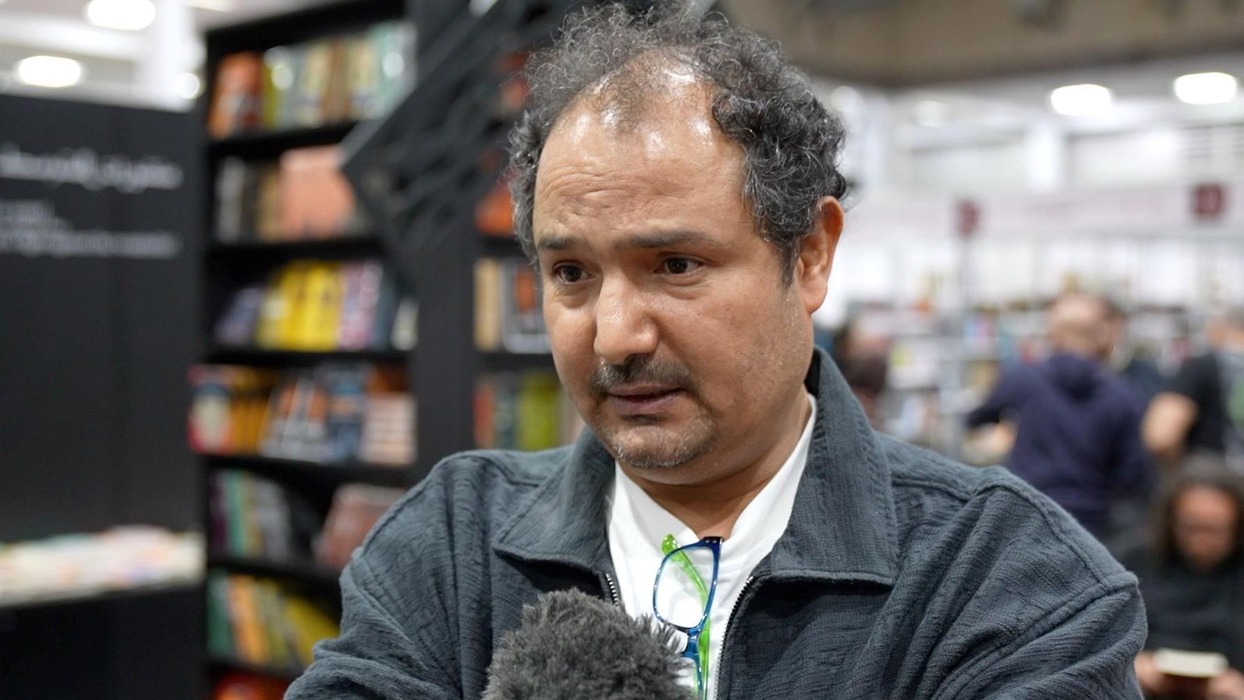 رجل يرتدي قميصاً داكن اللون يتحدث أمام مايكروفون